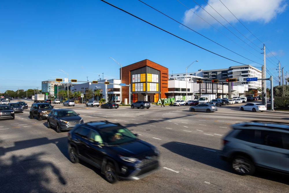 Cars driving through an urban intersection in front of a modern commercial building with an Atrium sign. South Florida Business & Wealth