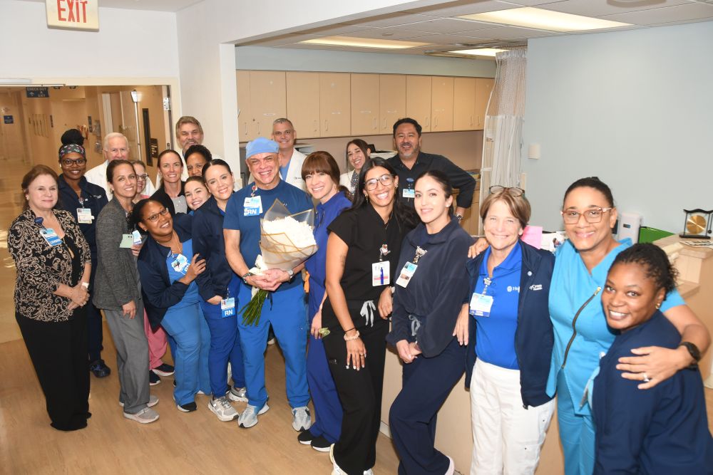 A large group of hospital staff posing together, with one nurse in the center holding a large bouquet of white flowers. South Florida Business & Wealth