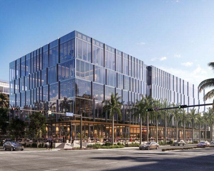 A modern multi-story office building with a glass facade, ground-floor retail spaces, and surrounding palm trees on a city street corner. South Florida Business & Wealth